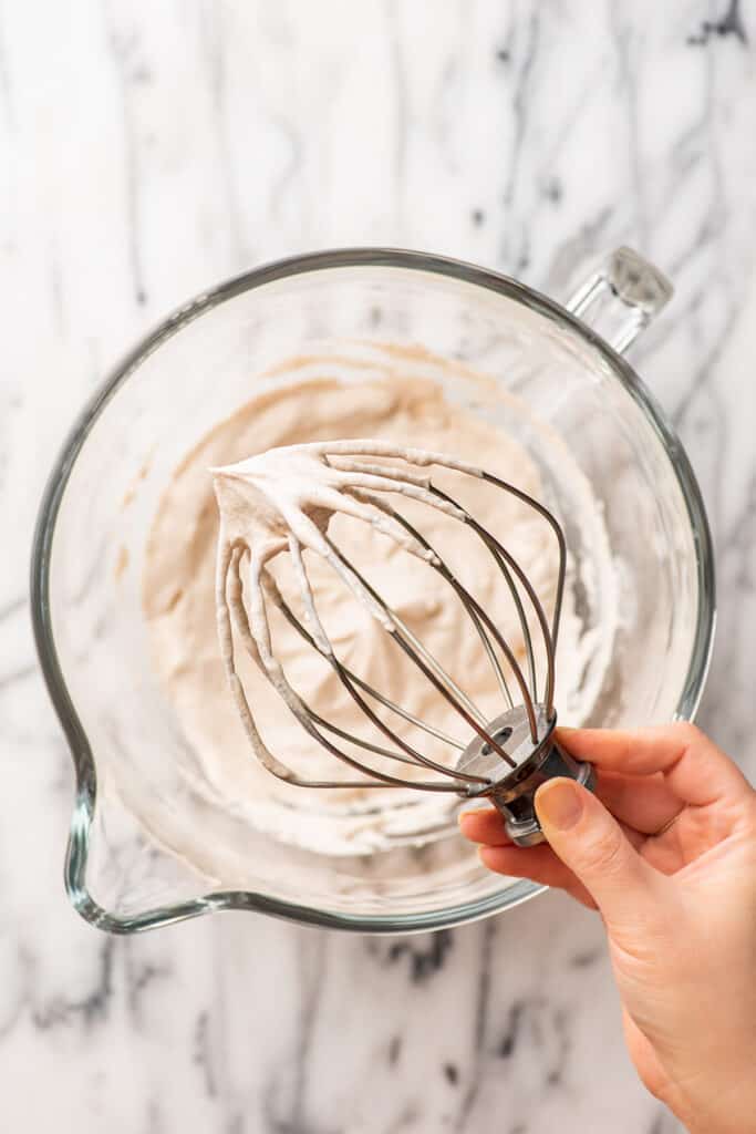 Cinnamon whipped cream on a whisk attachment over a stand mixer bowl.