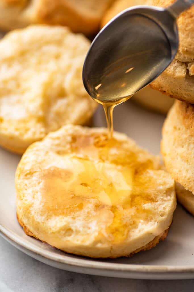 Broken open biscuit with butter being drizzled with honey.