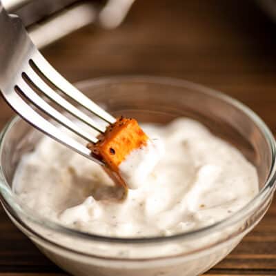 Sweet potato being dipped in greek yogurt aioli.