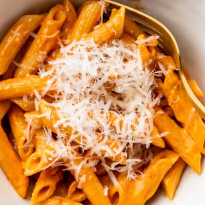 Penne alla vodka for one in a white bowl with Parmesan cheese.