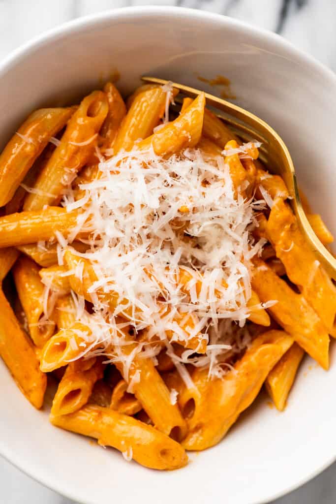 Penne alla vodka for one in a white bowl with Parmesan cheese.