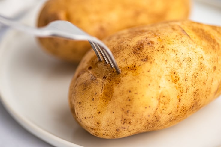 Potato being pierced with a fork before microwaving.