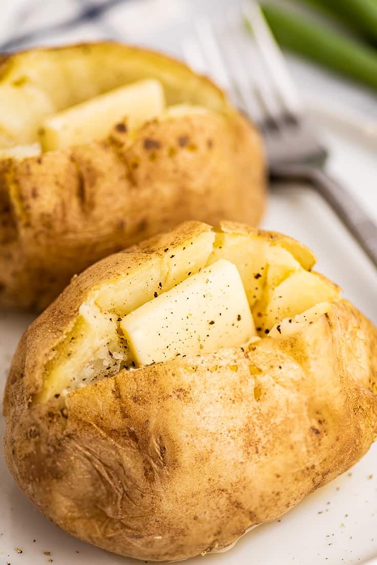 Microwave baked potatoes on a plate with butter.