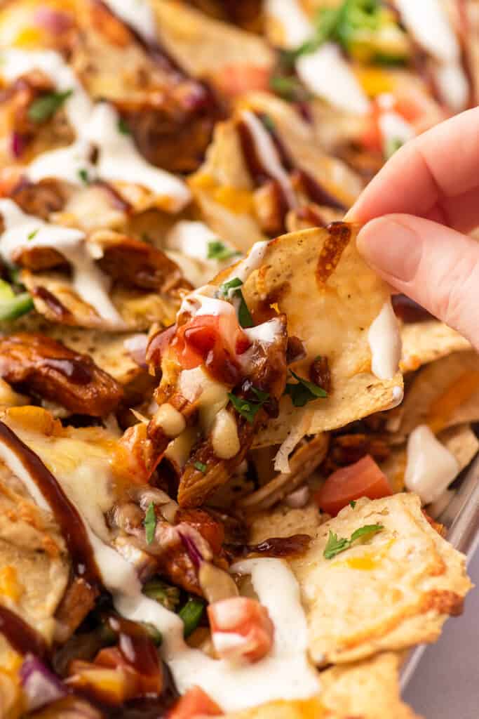 BBQ chicken nacho being picked up from a sheet pan.