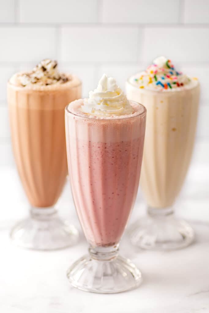 Strawberry, vanilla, and chocolate milkshake recipes in clear glasses.