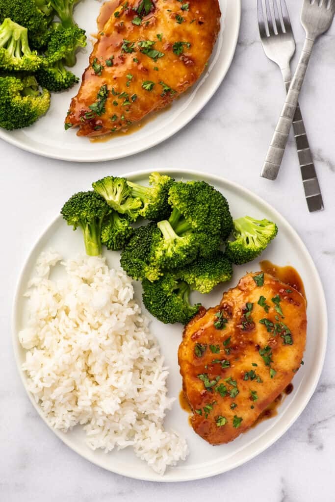 Two plates with honey garlic chicken, rice, and broccoli.