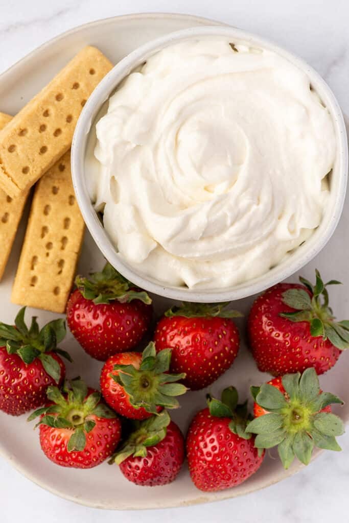 Bowl with cream cheese whipped cream next to strawberries.