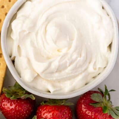 Bowl with cream cheese whipped cream next to strawberries.