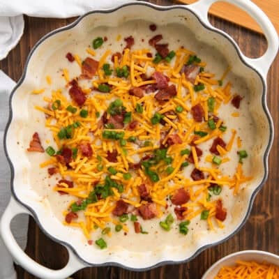 a pot of baked potato soup topped with bacon bits, scallions, and shredded cheddar cheese