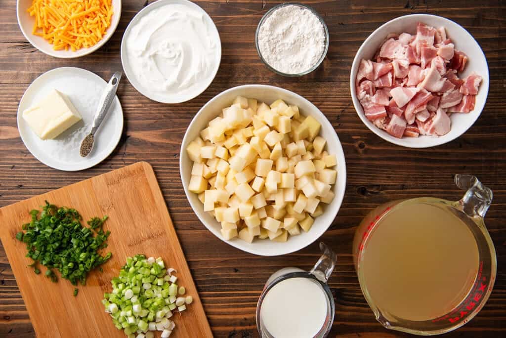 ingredients for a bowl of baked potato soup topped with bacon bits, green onions, and shredded cheddar cheese