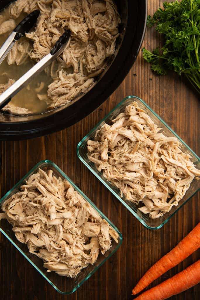 Slow cooker shredded chicken being stored in glass containers.