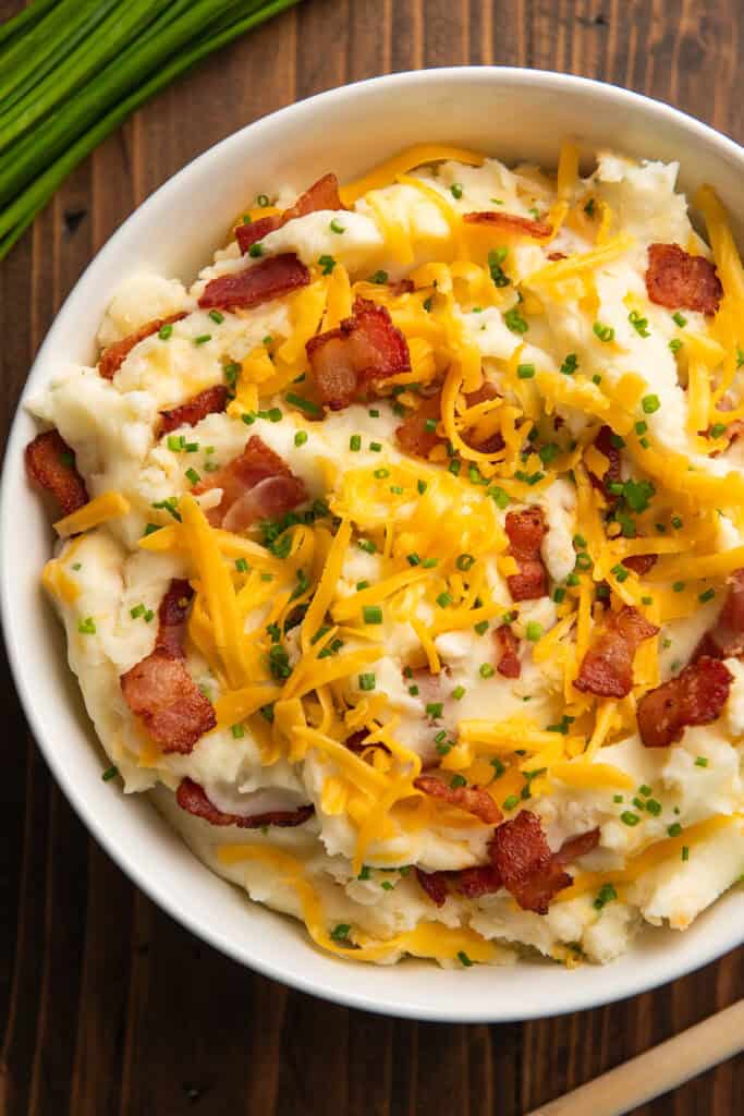 Close up picture of loaded mashed potatoes in a white bowl.