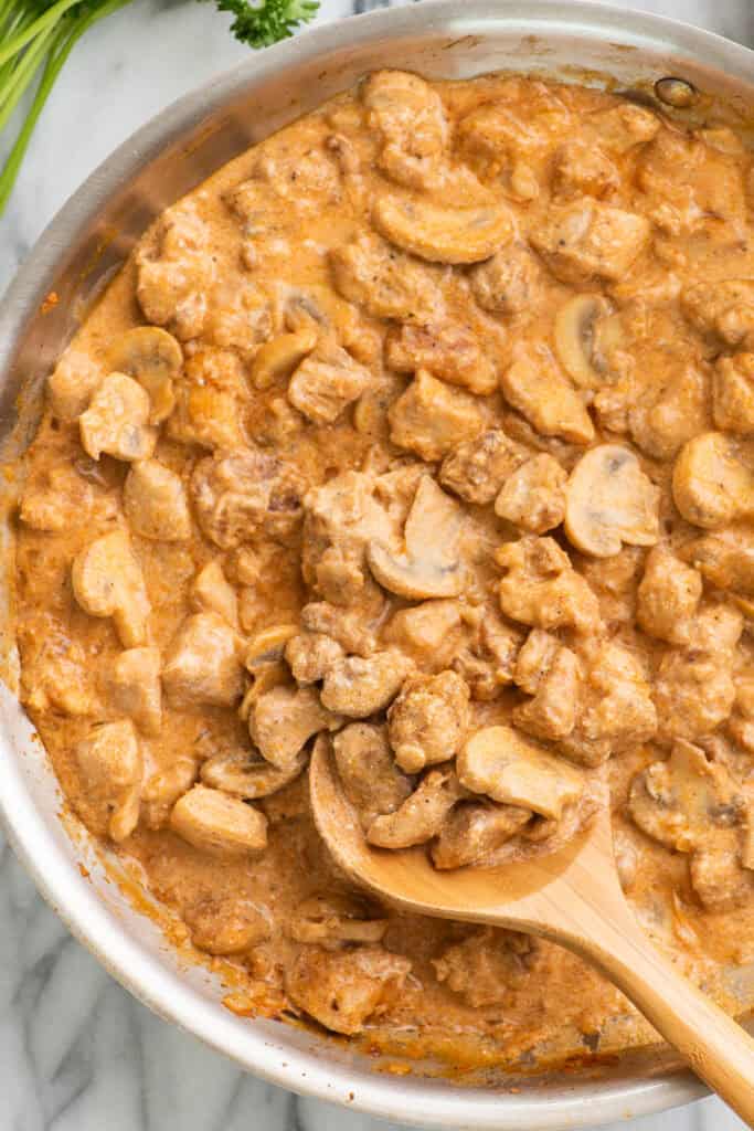 Close up of chicken stroganoff in a skillet with a wooden spoon