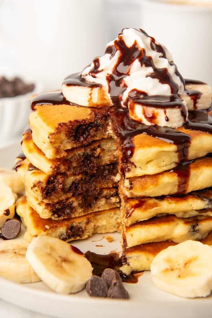 Close up photo of chocolate chip pancakes with whipped cream and chocolate sauce