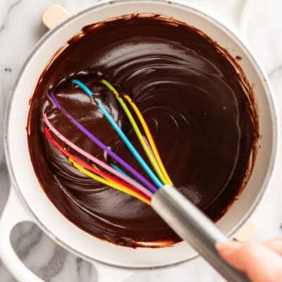 A hand whisking chocolate in a pan with a rainbow whisk.